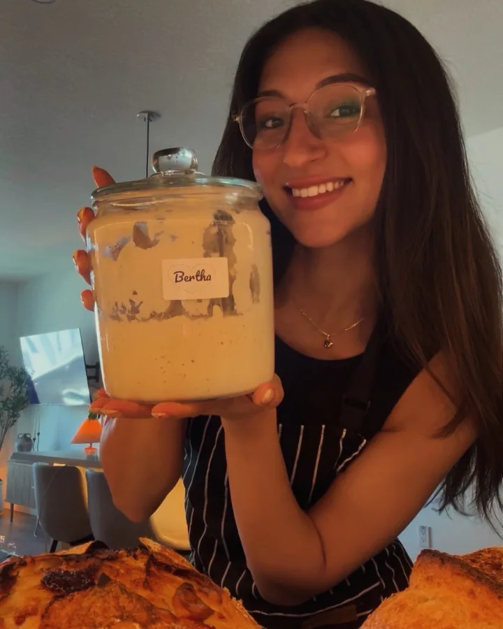 Sof holding up the glass jar labelled Bertha, two loaves cooling in front of her.