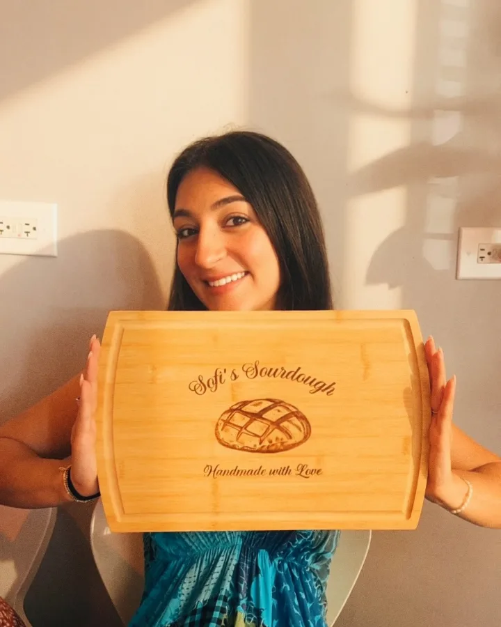 Sof holding a wooden board engraved Sofi&rsquo;s Sourdough, handmade with love.